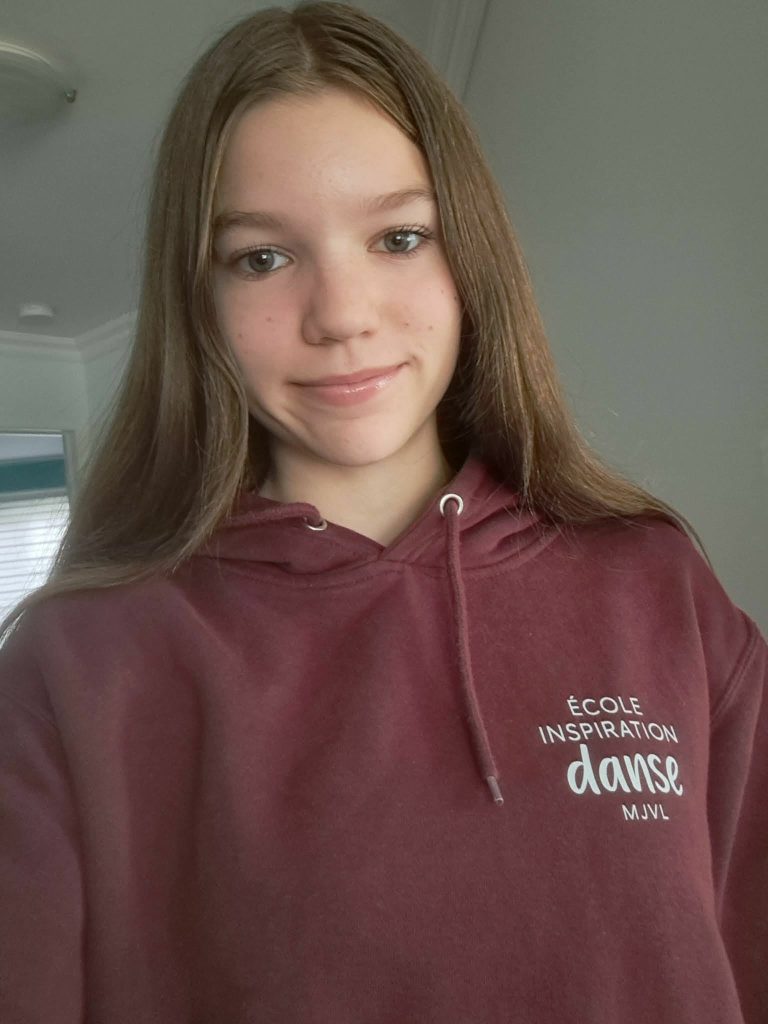 Fille d'environ 16 ans souriant à la caméra avec un chandail de Inspiration Danse